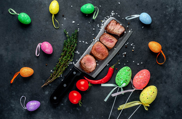 Grilled beef steak over a meat knife with spices and decorative Easter eggs. View from above. on a...