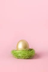 Golden egg in pink nest. Easter minimal creative composition on pastel pink with copy space. Close up. Happy Easter holiday. Greeting card.
