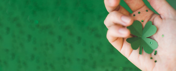 Saint Patricks day banner with top view of green four-leafed paper clover on womans hand sprinkled with small stars