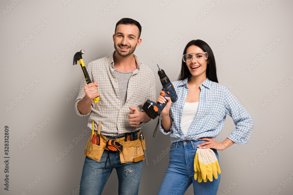 Wall mural excited manual workers holding hammer and electric drill on grey