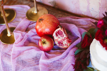 Whole and broken into pieces pomegranates are laid out on a pink fabric served with an apple on a rustic table