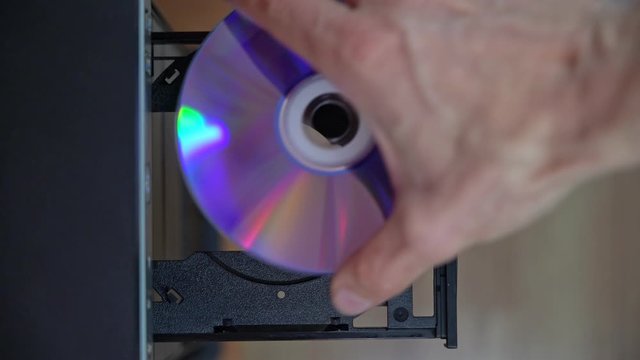 A male programmer inserts a CD-DVD from a computer drive. View from above. Outdated obsolete technology.