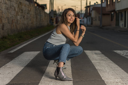 Pretty Latin Single Woman Portrait Outdoors Wearing Jeans Squatting Over Pedestrian Crosswalk . Selective Focus