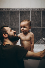 Fototapeta na wymiar selective focus, noise effect: bearded father is washing and bathing the baby in the bathroom, child girl have fun, she is happy and smiling, likes to enjoy water