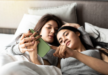 In selective focus of mobile phone was holding by love couple hands,blurred two women laying down on bed,with romantic feeling.