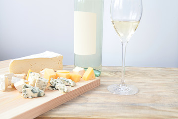 Bottle of white wine two glasses and cheese on a wooden board