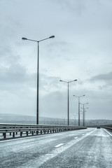 a road with white markings on the asphalt against a gray sky. Road fence