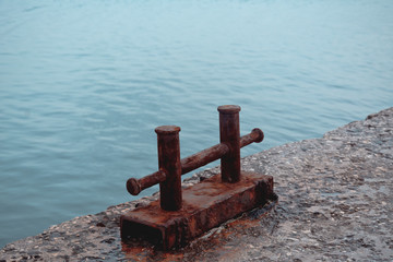Rusty steel double berth on a fragment of an old concrete pier against a background of turquoise sea water