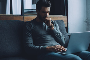 Handsome man with hand near mouth watching pornography on laptop in living room