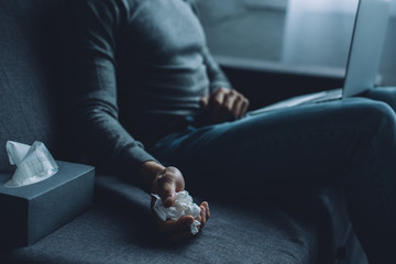Selective focus of man holding crumpled napkin while watching pornography on laptop on sofa