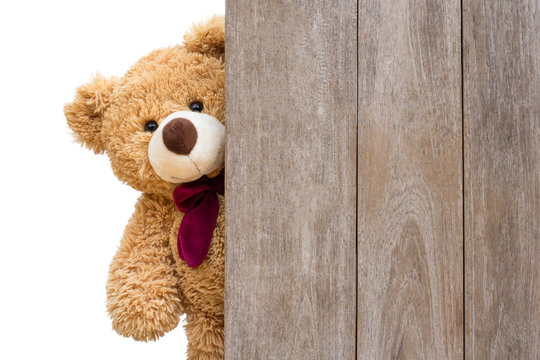 Naklejki Brown cute teddy bear sneaked behind the old wooden door isolated on white background. Copy space for text and content.