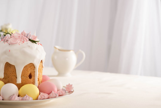 Delicious Easter cake decorated with meringue near pink and white eggs on plate
