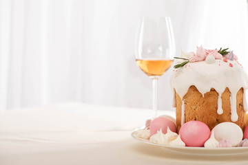 Delicious Easter cake decorated with meringue with pink and white eggs on plate near wine glass
