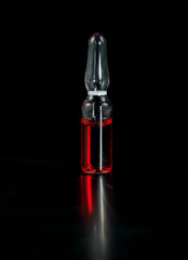 Ampule with red medicine a close-up on a black background