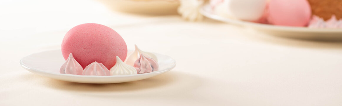 Pink painted Easter egg with meringue on plate, panoramic shot