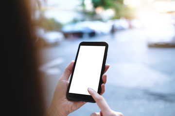 Closeup of male hand holding and using modern smart phone with blank screen for your text or content, with city bokeh