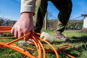 Gardener raising an extension cord. Homemade extension cord on the grass left by the gardener. Work in the home garden.
