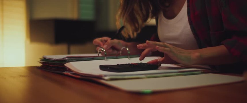 Young woman student studying at home in the evening, writing notes and calculating math. Close up. BMPCC 4K