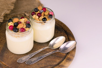  Two servings of yogurt with granola and berries on a wooden board. Copy space