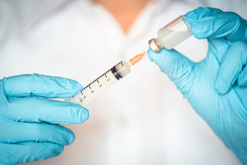 Doctor, nurse or scientist hand in blue nitrile gloves holding flu, measles, coronavirus vaccine shot for baby and adult vaccination, medicine and drug concept