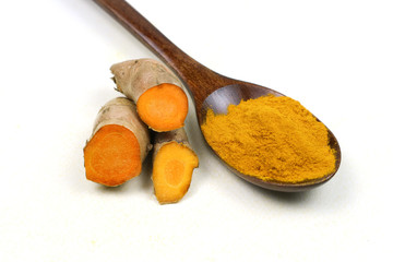 Turmeric powder in a wooden spoon and fresh turmeric roots isolated on a white background is an...