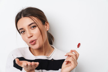 Image of young joyful woman holding lollipop and blowing air kiss