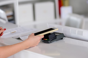 Young girl's hands are holding smartphone while receiving keys to hotel room for payment using contactless payment system. Concept of check-in at the hotel and modern means of payment