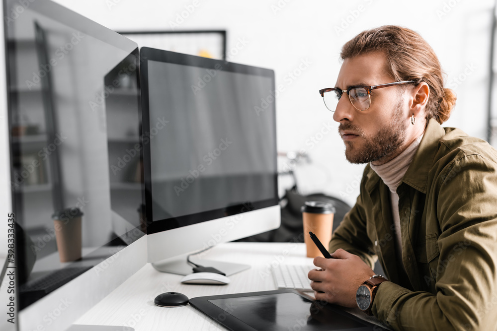 Poster side view of handsome 3d artist holding stylus near graphics tablet and looking at computer monitors