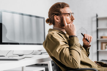 Pensive 3d artist holding stylus of graphics tablet near computer on working table
