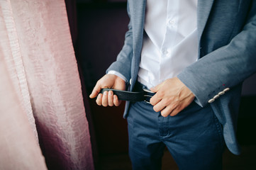Obraz na płótnie Canvas groom puts on a belt standing near window