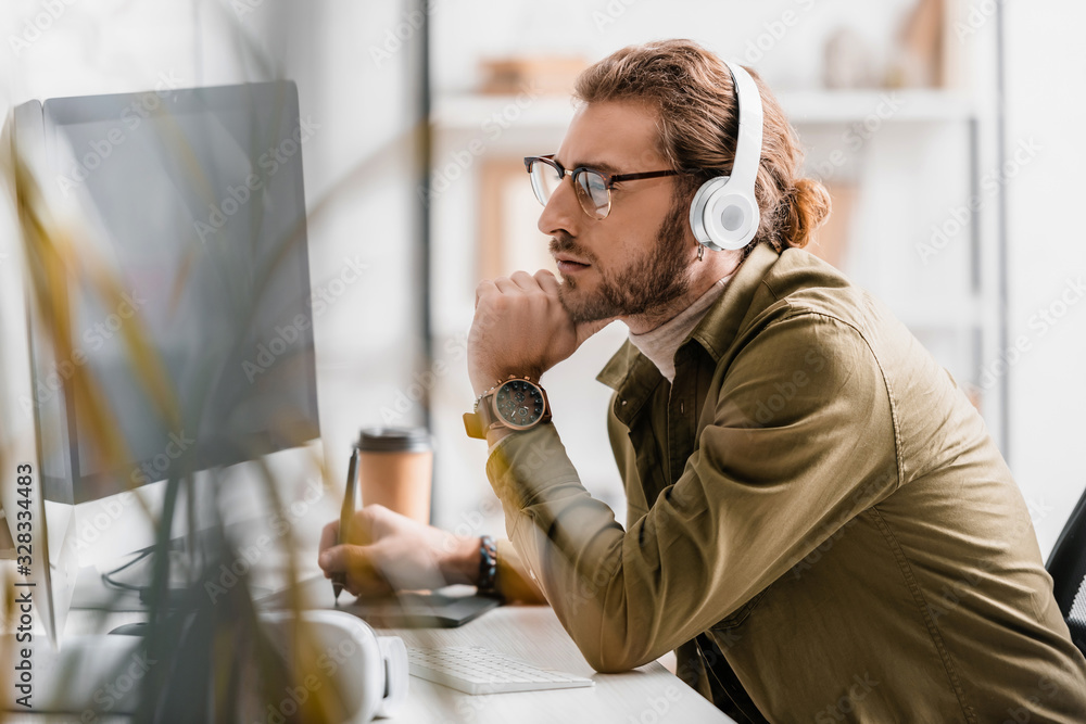 Poster side view of 3d artist in headphones using graphics tablet and looking at computer monitor on table