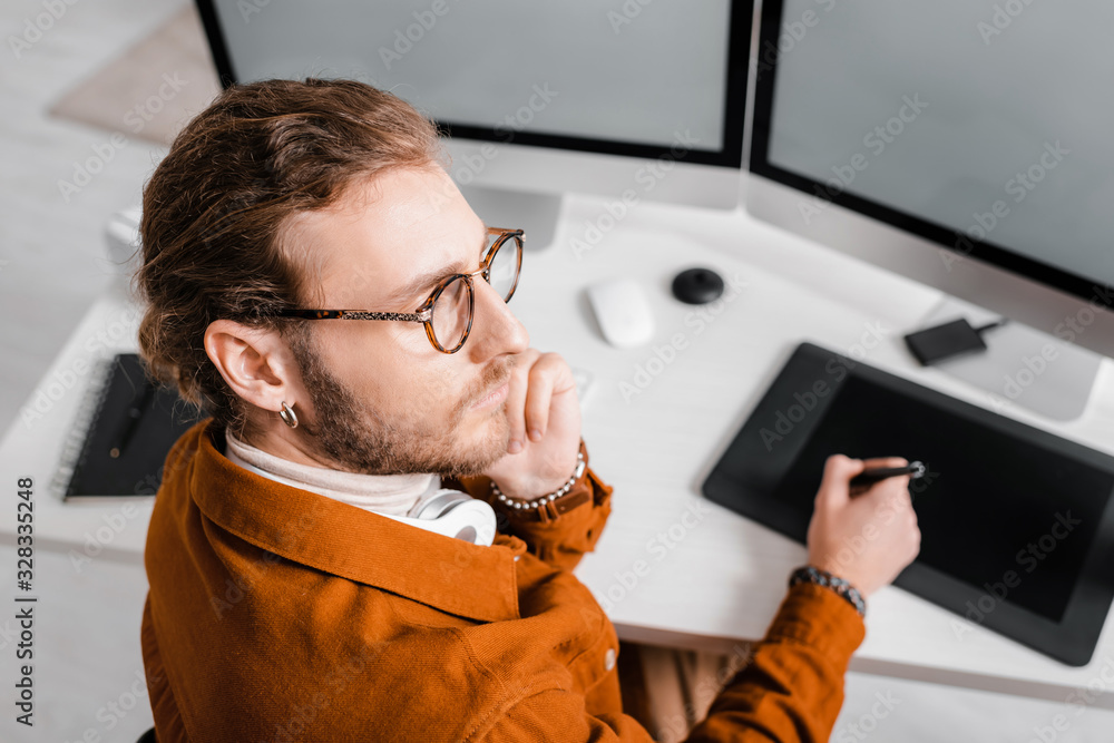 Poster selective focus of pensive 3d artist looking away while working with graphics tablet and computers a