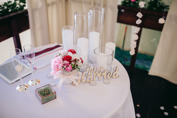 Set of wedding rings in glass box with succulents, candles, flowers and two glasses for champagne are on the round table covered with white tablecloth at the wedding ceremony area