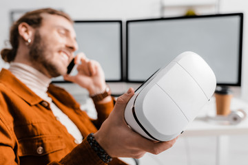 Selective focus of smiling 3d artist talking on smartphone and holding vr headset in office