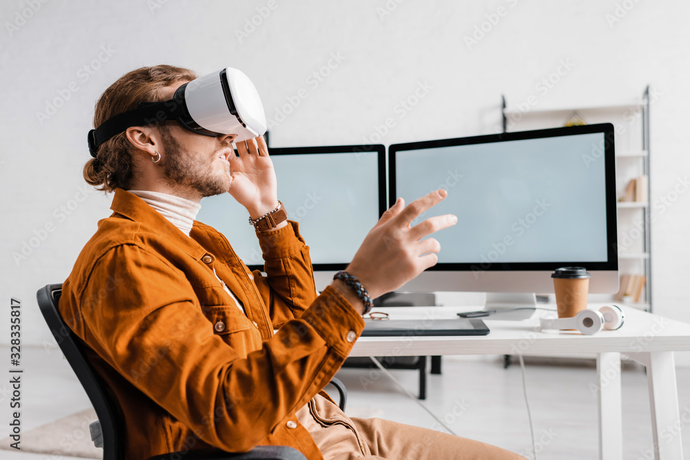 Poster side view of 3d artist gesturing while using vr headset near digital devices on table