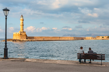 young couple in love sitting on a bench by the sea on the waterfront of the Greek city of Chania.