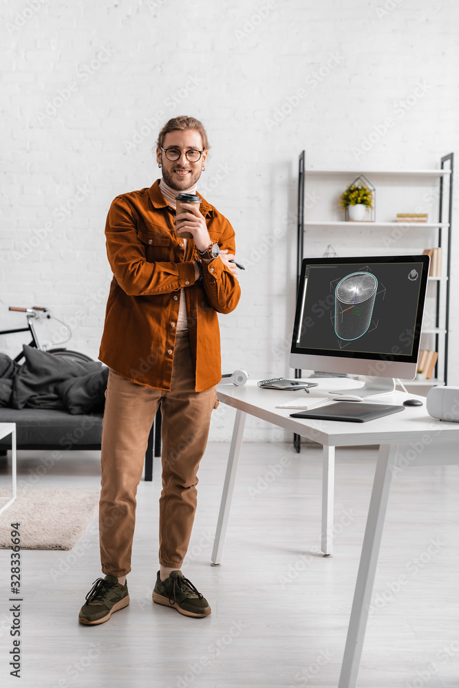 Poster smiling digital artist looking at camera while holding coffee to go near 3d design project on comput