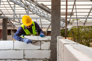 Naklejka na ściany i meble bricklayer builder working with autoclaved aerated concrete blocks. Walling, installing bricks on construction site, Engineering and constructions concepts.