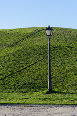Lighthouse off light placed on the side of a green hill on a bright sunny morning