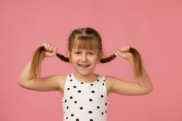 Cute small child girl holding long hair braids on pink background. Braiding hair.