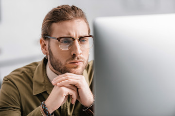 Selective focus of pensive 3d artist looking at computer monitor in office