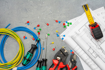Tools and tips of different sizes and colors for crimping stranded electrical wires. Crimping tools, wire tips and electrical cable on a grey concrete background	
