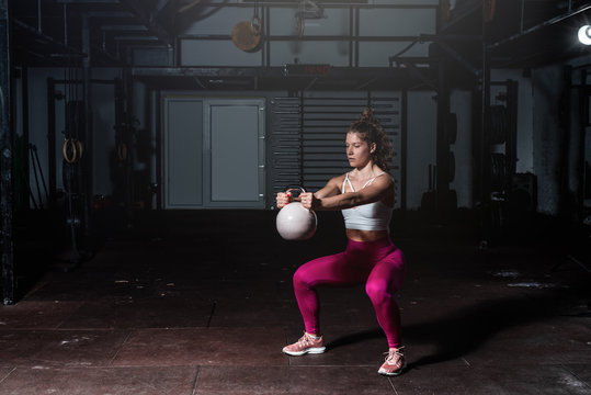 Young sweaty fit muscular strong girl doing hardcore cross workout training for shoulder muscles with heavy kettlebell in the gym dark image real people exercising