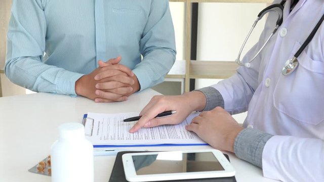 4k video of patient listening intently to a male doctor explaining patient symptoms or asking a question as they discuss paperwork together in a consultation.