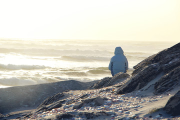 Person sitting on the rocks by the oceans watching the waves during sunset