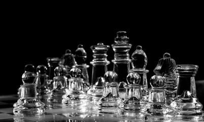 Full set of clear, transparent glass chess pieces or figures arranged on chessboard and ready for...