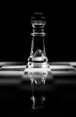 Single clear glass king chess piece or figure standing on glass chessboard with reflection. Isolated on black background with copy space. Black and white photography.