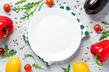 Healthy food. Vegetables, lemon and chickpeas around empty white plate on a concrete background, top view, free space for text. Vegetarian and vegan food concept, copy space, flat lay.