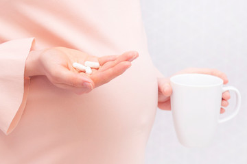 Close-up of pregnant woman holding a pill, vitamins. The concept of pregnancy, healthcare, gynecology, medicine and a healthy lifestyle. Mother is expecting a baby. Nutritional supplements.