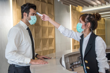 Staff woman wear protective masks at the counter used the digital thermometer to measure the...
